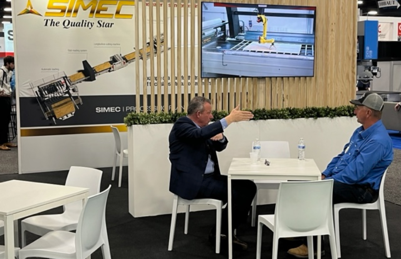 2 men sitting at a table discussing a machine at a conference