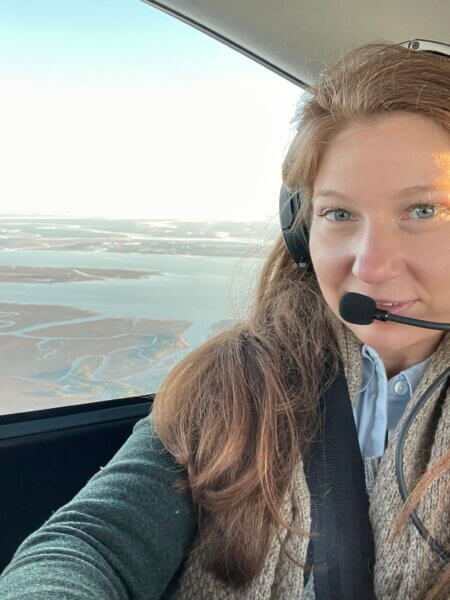 Sydney in a plane with headset on looking out the window